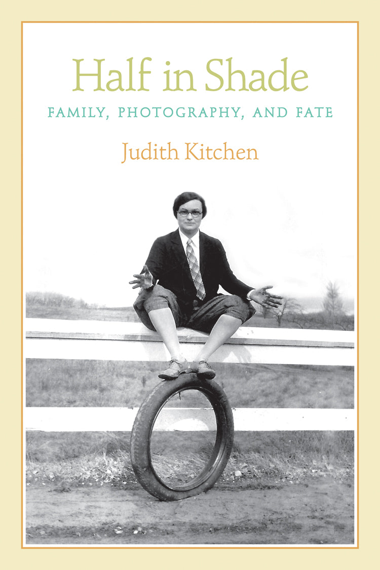 Cover of "Half in Shade," by Judith Kitchen, which is an black and white photograph of a lady sitting on a fence, wearing a suit, and has her feet propped on a tire. 